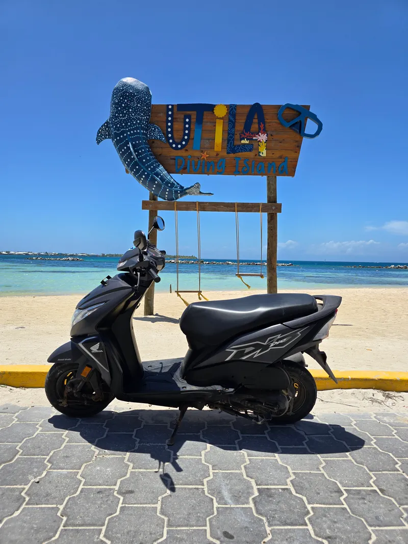 A scooter parked by the Utila Diving Island sign on the waterfront